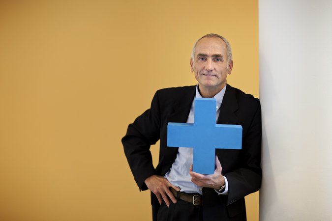 Mann im Sacko hält blaues Erasmus Plus Symbol in die Kamera
