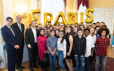 Gruppenfoto von dem österreichischen Bildungsminister und einer Schulkasse in einem Raum. Im Hintergrund sit das Wort Erasmus mit Ballonen geschrieben.