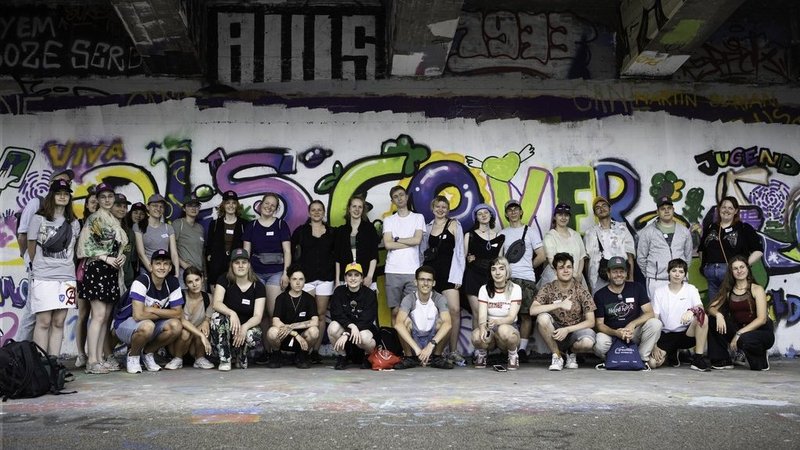 Eine Gruppe von über 30 jungen Menschen steht vor einer Wand, die mit Graffiti besprüht wurde