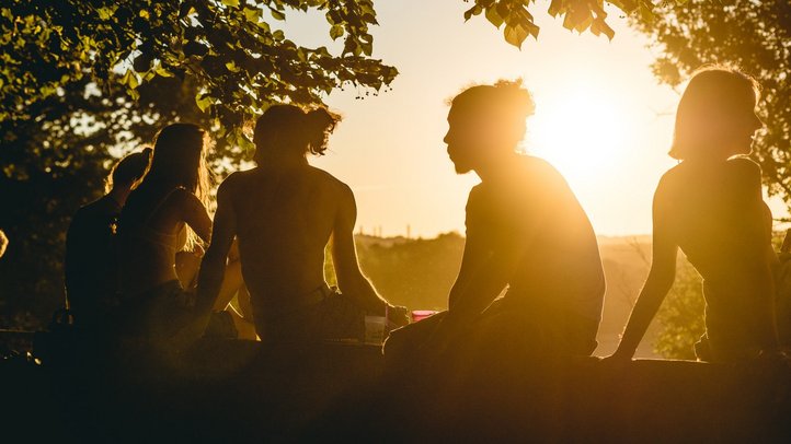 Jugendliche sitzen im Sonnenuntergang am Baum