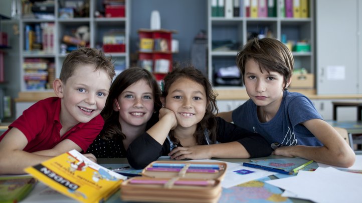 Kinder lächeln für ein Gruppenfoto in die Kamera, vor ihnen liegen Bücher