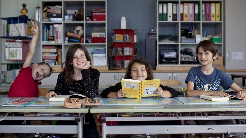 Zwei Mädchen und zwei Buben sitzen auf ihrem Platz in einem Klassenzimmer und blicken in die Kamera