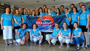 Gruppe an Menschen mit 30 Jahre Erasmus+ T-Shirt gekleidet halten gemeinsam die 30 Jahre Erasmus+ Flagge hoch