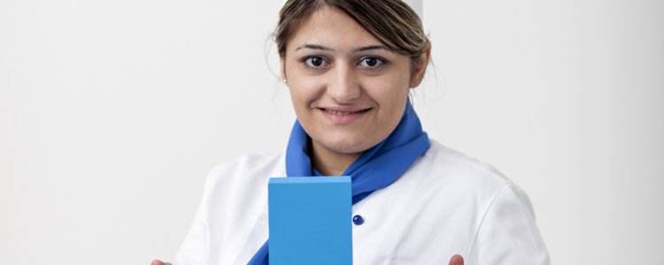 Junge Frau mit weißer Kochmütze hält blaues Erasmus-Logo in die Höhe