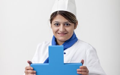 Junge Frau mit weißer Kochmütze hält blaues Erasmus-Logo in die Höhe