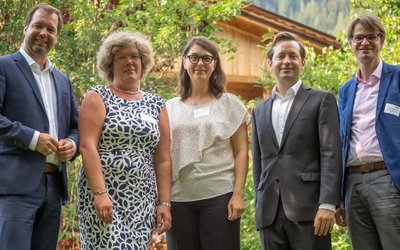 5 Personen (darunter Ernst Gesslbauer, Leiter der Nationalagentur Erasmus+ Bildung und Jakob Calice, Geschäftsführer des OeAD) stehen auf einer Wiese mit grünen Büschen und einem Holzhaus im Hintergrund