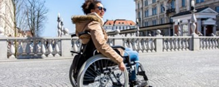 Junge Frau fährt mit Rollstuhl über eine Brücke