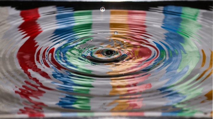 Wassertropfen auf Wasser, an der Wasseroberfläche spiegeln sich verschiedene Farben