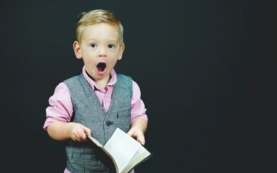 EIn blinder junge im Kindergartenalter hält ein aufgeschlagenes Buch in der Hand, ist erstaunt und hat den Mund weit offen.