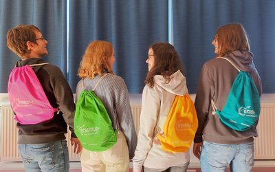 Vier Schülerinnen und Schüler stehen mit dem Rücken zur Kamera und tragen Erasmus+ Turnsäcke