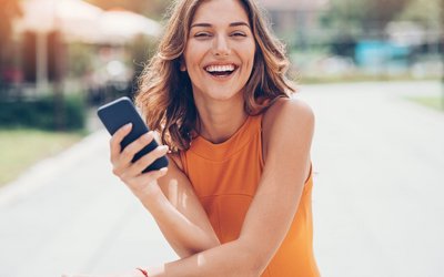 Eine Frau mit einem Telefon in der Hand lacht in die Kamera