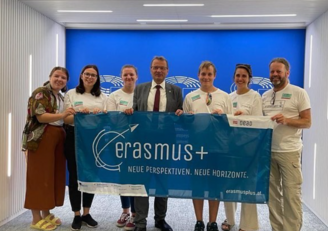 Gruppe an sieben Menschen hält Erasmus+ Banner in die Kamera