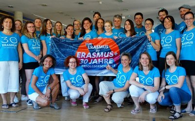 Gruppe an Menschen mit 30 Jahre Erasmus+ T-Shirt gekleidet halten gemeinsam die 30 Jahre Erasmus+ Flagge hoch